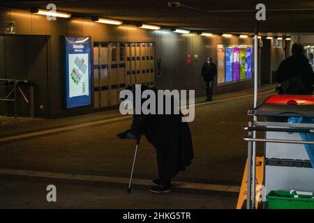 Bettlerin in einem Tunnel zum Bahnhof. Sie trägt eine Covid-Maske und sticht eine Hand heraus. In der anderen Hand hält sie eine Krücke. Stockfoto