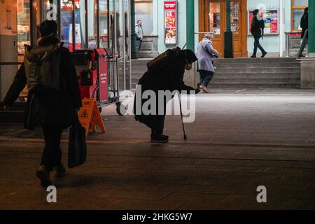 Bettlerin in einem Tunnel zum Bahnhof. Sie trägt eine Covid-Maske und sticht eine Hand heraus. In der anderen Hand hält sie eine Krücke. Stockfoto