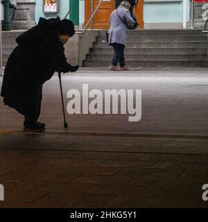 Bettlerin in einem Tunnel zum Bahnhof. Sie trägt eine Covid-Maske und sticht eine Hand heraus. In der anderen Hand hält sie eine Krücke. Stockfoto