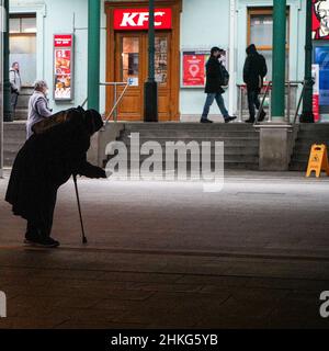 Bettlerin in einem Tunnel zum Bahnhof. Sie trägt eine Covid-Maske und sticht eine Hand heraus. In der anderen Hand hält sie eine Krücke. Stockfoto