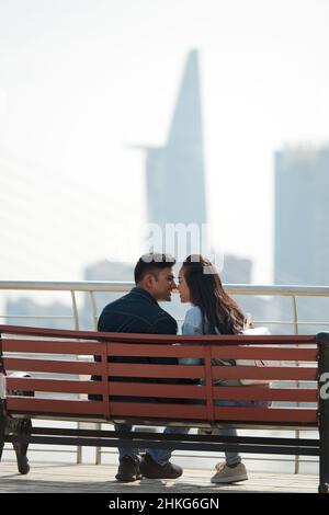 Junges Paar in Liebe küssen, wenn auf der Bank mit Blick auf schöne Stadtlandschaft sitzen Stockfoto