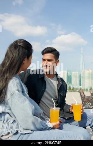 Glückliches junges Paar, das Zeit auf dem Flussembargo verbringt, auf der Bank sitzt, spricht und weiche Fransen hat Stockfoto