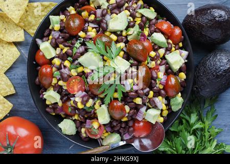 Hausgemachter mexikanischer Salat mit schwarzen Bohnen und Mais oder texanisches Kalksandressing mit Kaviarbohnendip, serviert mit Tortilla-Chips und frischen Zutaten. Stockfoto