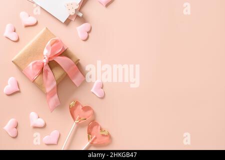 Valentinstag Grußkarte mit Geschenk, Liebesbrief, zwei Süßigkeiten Lutscher und rosa Herzen auf rosa Hintergrund. Blick von oben. Platz für Text. Flat la Stockfoto
