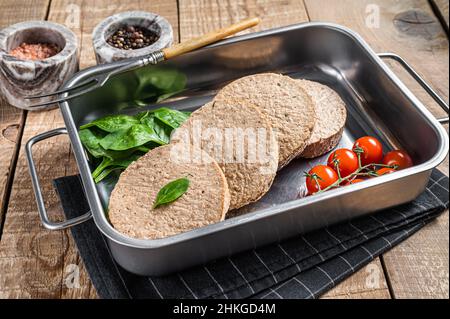 Rohe, fleischfreie Patties aus Fleisch auf pflanzlicher Basis, frische vegane Burger-Cutlets in Küchentablett mit Kräutern. Holzhintergrund. Draufsicht Stockfoto