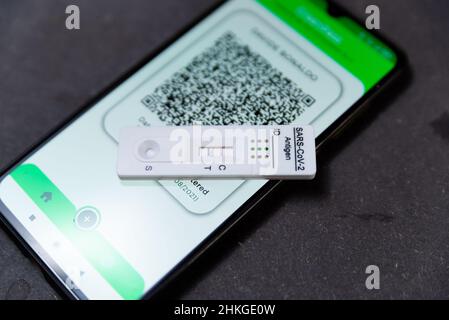 Ein positiver Covid-Schnelltest, auch Antigentest oder Lateral-Flow-Test genannt, wird in einer Nahaufnahme auf einem Tisch zusammen mit einem Handy-Showin gesehen Stockfoto