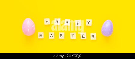 Grußkarte mit Text Frohe Ostern. Bunte ostereier und Papierkaninchen auf gelbem Hintergrund Stockfoto