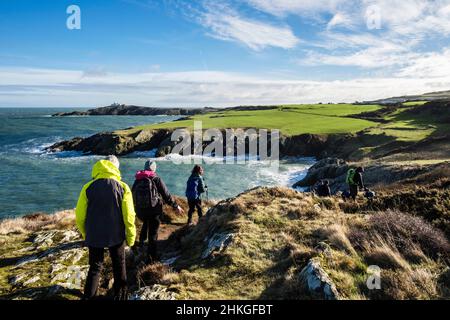 Spaziergänger, die von Amlwch nach Llaneilian auf dem Anglesey Coastal Path wandern, mit Blick entlang der felsigen Küste bis zum Point Lynas. Isle of Anglesey, Nordwales, Großbritannien Stockfoto