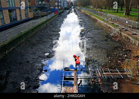 Ein Bauarbeiter baut eine Plattform auf dem entwässerten Hertford Union Canal in der Nähe des Victoria Parks im Osten Londons. Der Kanal, der den Regent's Canal mit der Lee Navigation verbindet, ist fast 200 Jahre alt und ein Abschnitt wurde drei Monate lang geschlossen und abgepumpt, damit an seinen Wänden wesentliche Reparaturarbeiten durchgeführt werden können. Bilddatum: Freitag, 4. Februar 2022. Stockfoto