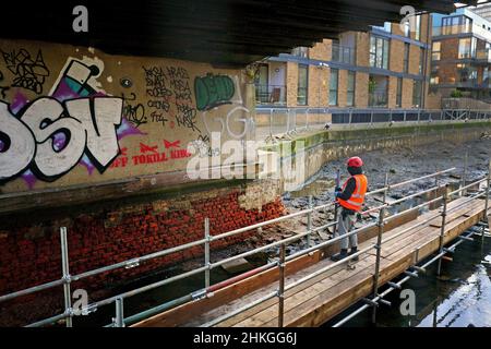 Ein Bauarbeiter baut eine Plattform auf dem entwässerten Hertford Union Canal in der Nähe des Victoria Parks im Osten Londons. Der Kanal, der den Regent's Canal mit der Lee Navigation verbindet, ist fast 200 Jahre alt und ein Abschnitt wurde drei Monate lang geschlossen und abgepumpt, damit an seinen Wänden wesentliche Reparaturarbeiten durchgeführt werden können. Bilddatum: Freitag, 4. Februar 2022. Stockfoto