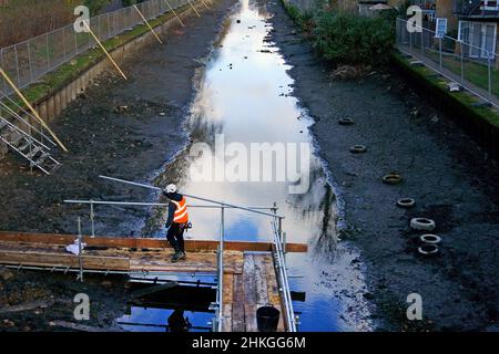 Ein Bauarbeiter baut eine Plattform auf dem entwässerten Hertford Union Canal in der Nähe des Victoria Parks im Osten Londons. Der Kanal, der den Regent's Canal mit der Lee Navigation verbindet, ist fast 200 Jahre alt und ein Abschnitt wurde drei Monate lang geschlossen und abgepumpt, damit an seinen Wänden wesentliche Reparaturarbeiten durchgeführt werden können. Bilddatum: Freitag, 4. Februar 2022. Stockfoto