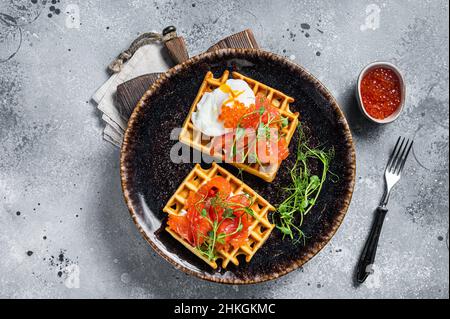 Belgische Waffeln mit Frischkäse, Lachsscheiben, Ei und rotem Kaviar. Grauer Hintergrund. Draufsicht Stockfoto