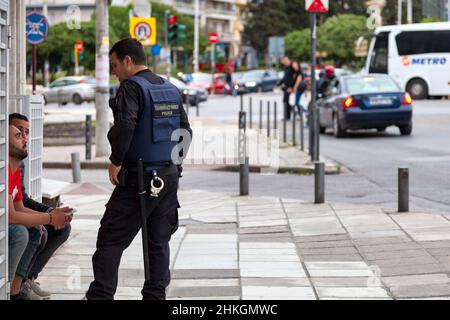 Thessaloniki, Griechenland - 03 2019. Mai: Ein Polizist, der mit zwei Männern spricht, sitzt auf der Türstufe eines Gebäudes im Stadtzentrum. Stockfoto