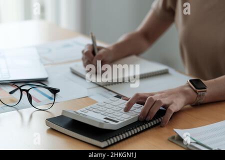 Close up Hand of Accounting zeichnet die Finanzwachstumsstatistiken des Unternehmens auf, wobei Grafiken als Referenz für die Überprüfung und Analyse der Ergebnisse verwendet werden Stockfoto