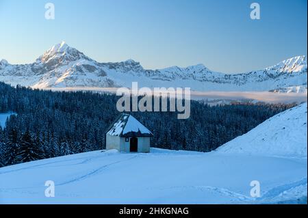 Ein kleines Häuschen im Schnee vor dem riesigen Berg der französischen Alpen-Bergkette. Stockfoto