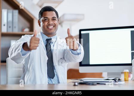 Sie sehen schon jetzt viel besser aus. Porträt eines jungen Arztes, der in seinem Büro Daumen nach oben zeigt. Stockfoto