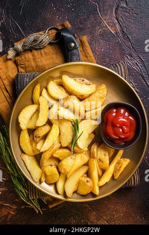 Gewürzte Kartoffelkeile mit Rosmarin- und Tomatensauce auf einem Teller. Dunkler Hintergrund. Draufsicht Stockfoto