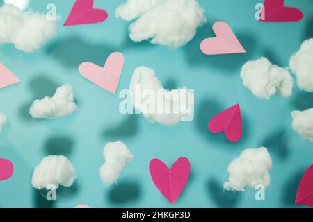 Pinke Herzen fliegen auf einem pastellblauen Hintergrund zwischen weißen Baumwollwolken. Stockfoto