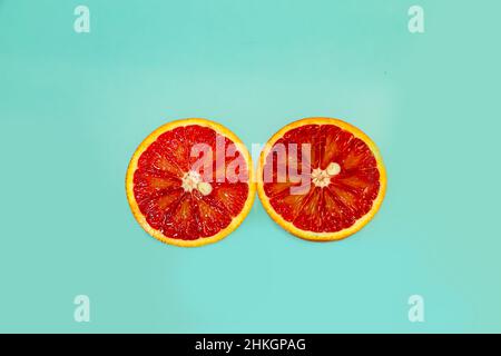Ganze und in Scheiben geschnittene saftige rote Orangen auf blauem Hintergrund. Hintergrund der Speisen. Stockfoto