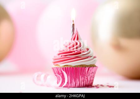 Pinker Geburtstagskuchen mit einer goldenen Kerze vor einem Hintergrund aus rosa und goldenen Luftballons Stockfoto