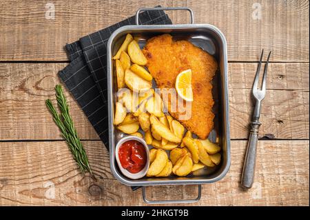 Schweinefleisch weiner Schnitzel mit Kartoffelkeilen und Tomatensauce in Stahlblech. Holzhintergrund. Draufsicht Stockfoto