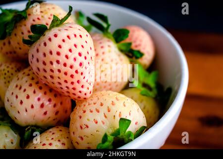 Frische weiße Weinbeeren mit Wassertropfen: Nahaufnahme von ganzen feuchten weißen Erdbeeren in einer Keramikschale Stockfoto
