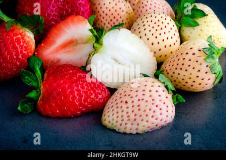 Nahaufnahme Ansicht von reifen Pinebeeren und Erdbeeren: Ganze und halbierte rote und weiße Erdbeeren auf dunklem Hintergrund Stockfoto