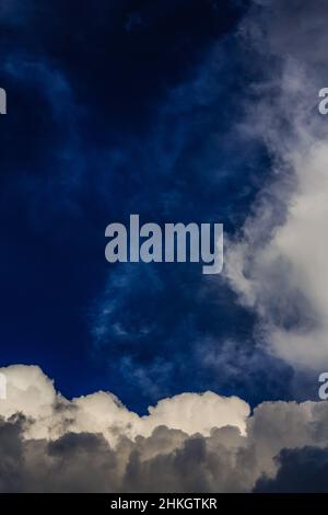 Höchst ungewöhnliche Wolkenformationen, die in wabendem, lebhaftem Blau, Weiß und Grau und schwachen weißen Wölkchen kollidieren. Stockfoto