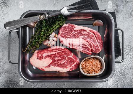 Ungekochte rohe Chuck Eye Roll Steaks in einer Stahlküchenschale. Grauer Hintergrund. Draufsicht Stockfoto