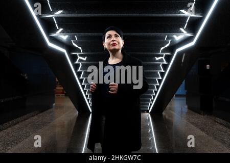 Eine elegante Frau in stilvollem Outfit posiert neben den leuchtenden Stufen. Stockfoto