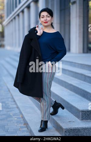 Eine elegante Frau in stilvollem Outfit posiert auf einer Stadtstraße. Stockfoto