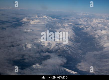 Blick auf schneebedeckte felsige Berge Kanadas zwischen Alberta und British Columbia vom Fensterplatz des Flugzeugs auf klaren Wintertagen Stockfoto