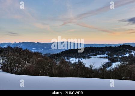Winter Berglandschaft in der Dämmerung. Kurz nach Sonnenuntergang. Mit Wald und Hügeln. Himmel in blauem Oange. Natur Hintergrund, Tapete. Vrsatec, Slowakei. Stockfoto
