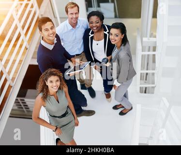 Erfolg, wir kommen für Sie. Porträt einer Gruppe lächelnder Mitarbeiter, die in einem modernen Büro auf einer Treppe stehen. Stockfoto