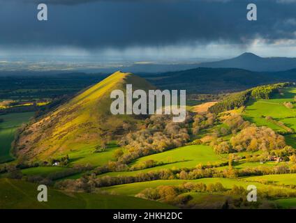 Abendlicht auf dem Lawley Hill, von Caer Caradoc aus gesehen, mit dem Wrekin im Schatten am Horizont, Shropshire. Stockfoto