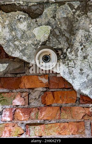 Beschädigtes Licht ohne Glühbirne an einer zerstörten Wand. Stockfoto