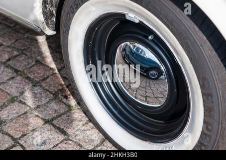 Nahaufnahme eines Oldtimer-Reifens mit verchromter Radkappe und Spiegelbild eines anderen deutschen Oldtimers, das darin zu sehen ist. Stockfoto
