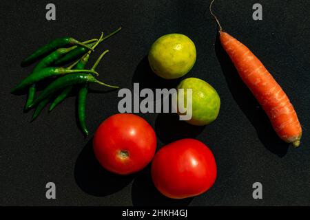 Tomaten, Zitronen, grüne Chilis und Karotten auf einem isolierten schwarzen Hintergrund angeordnet Stockfoto