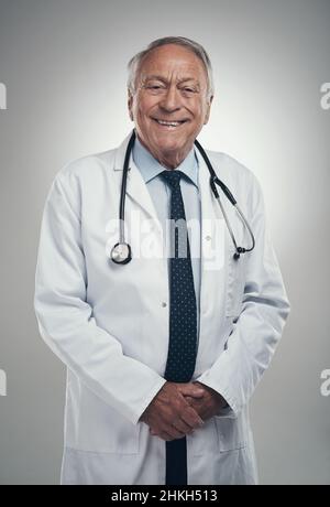 Nicht alle Helden tragen Umhänge. Aufnahme eines älteren männlichen Arztes in einem Studio vor grauem Hintergrund. Stockfoto