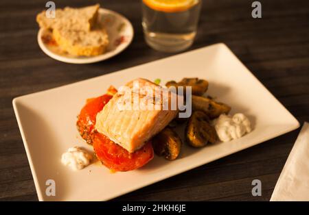 Gedünstetes Meerforellenfilet auf gebratenen Pilzen mit Tomaten auf einem weißen Teller serviert Stockfoto