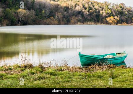 Ein helles smaragdgrünes Boot am Ufer eines ruhigen Sees an einem sonnigen Wintertag. Stockfoto
