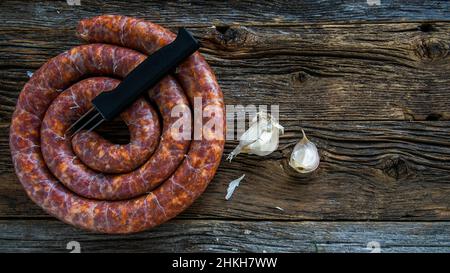 Hausgemachte traditionelle slowakische Wurst mit Knoblauch und Wurstpricker auf rustikalem Holzhintergrund Stockfoto