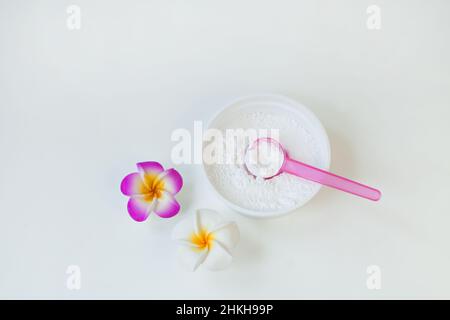 Kosmetisches weißes Pulver mit Löffel in Kunststoffbehälter in der Nähe von Frangipani Blume oder Protein-feinen Körnern Stockfoto