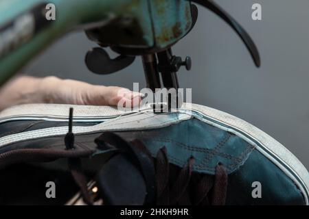 Turnschuhe reparieren. Mann repariert einen Sneaker mit einer Nähmaschine. Handwerkliches Werkstattkonzept. Stockfoto