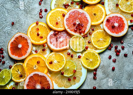 Diagonale Zusammensetzung aus Zitronenlistensaft, Zitrone, Limette, Orange und Granatapfelkernen auf einem rustikalen beigen Zementhintergrund, Draufsicht. Stockfoto