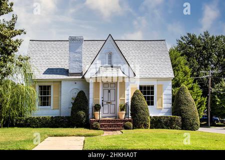 Niedliche gelbe und weiße Backstein- und Abstellhütte mit hübschem Rasen und Landschaftsgestaltung und Fensterläden in einer grünen Nachbarschaft. Stockfoto