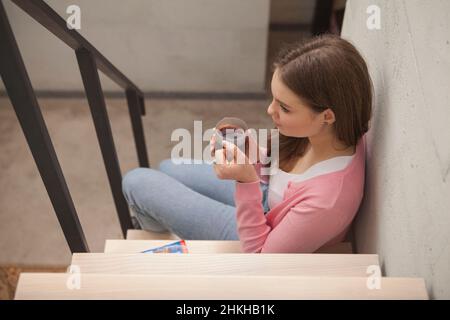 Draufsicht auf eine wunderschöne Frau, die Tee trinkt und auf der Treppe in ihrer Wohnung sitzt Stockfoto