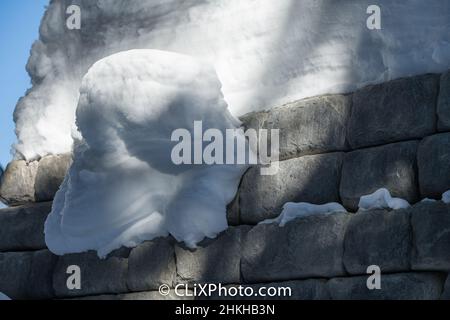 Schneeverwehung hängt an der von Menschen hergestellten Betonziegelwand rechteckige Ziegelsteine gestapelt außen Stützmauer mit schweren Schneelast horizontal Stockfoto