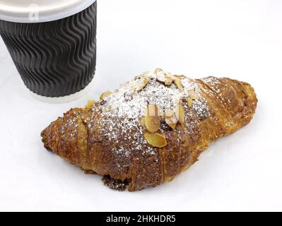 Mandelcroissant mit einer Papiertasse Kaffee auf weißem Hintergrund. Croissant mit Mandelflocken und Puderzucker mit einer Papiertasse. Leckeres Frühstück Stockfoto
