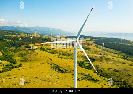 Leistungsstarke Windgeneratoren am Kraftwerk produzieren saubere Energie auf wilden Hochlandhügeln in der Nähe der Adria gegen die Berge aus der Luft Stockfoto